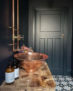 a copper bowl sink sitting on top of a wooden table next to a black door