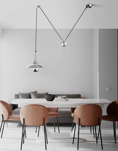 a dining room table with six chairs and a couch in the background, along with two lamps hanging from the ceiling