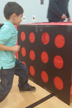 a young boy standing next to a giant red and black board game on top of a wooden floor