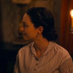 a woman sitting in front of a table with candles on the wall behind her and looking off to the side