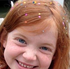 a close up of a child smiling with confetti on her head