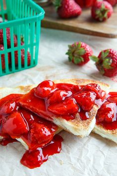 two pieces of toast with strawberry jam on them and some strawberries in the background