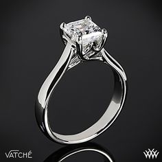 a white gold ring with a princess cut diamond in the center on a black background