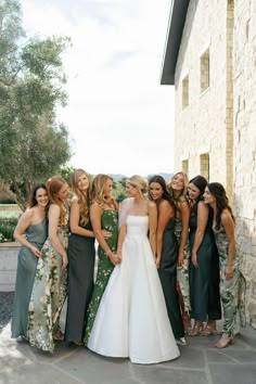 a group of women standing next to each other in front of a stone building with trees