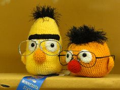 two crocheted stuffed animals with glasses on top of a wooden shelf next to each other