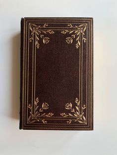 a brown book with gold trim sitting on top of a white table