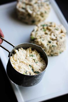 a person holding a ladle with some food in it on a white tray next to two cookies