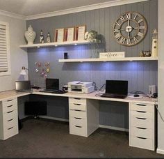 a desk with two laptops and a clock on the wall above it in a home office