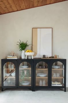 a glass cabinet with plates and bowls on it in front of a wall mounted art piece