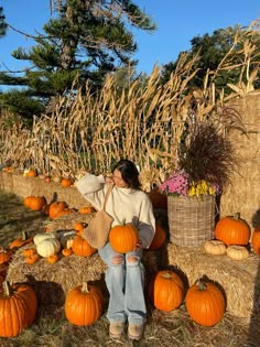 a woman sitting on hay bales surrounded by pumpkins