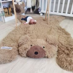 a teddy bear laying on the floor next to a crib with a baby in it