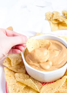 a person dipping some tortilla chips into a bowl with salsa in it on a plate