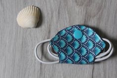 a blue and white face mask sitting on top of a wooden floor next to a seashell