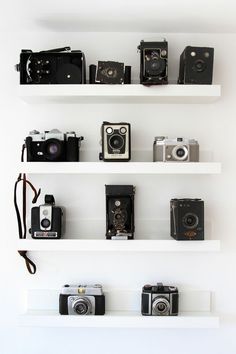 several cameras are lined up on white shelves