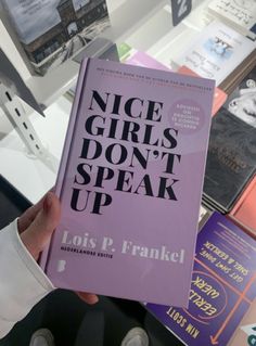 a person holding up a purple book in front of bookshelves with the words nice girls don't speak up