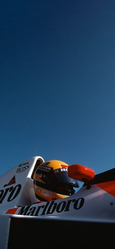 an orange and white race car driving on a track with blue sky in the background