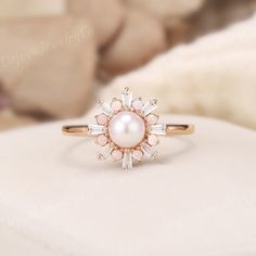 a pink pearl and diamond ring sitting on top of a white pillow