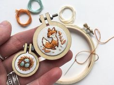 a hand is holding two small embroidered hoops