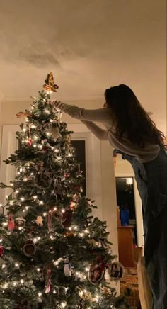 a woman decorating a christmas tree in her living room