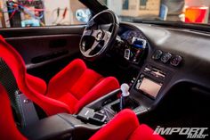 the interior of a sports car with red seats and steering wheel, including an electronic display