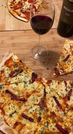 two slices of pizza sitting on top of a wooden table next to a glass of wine