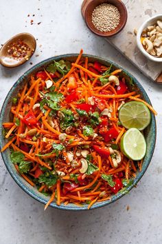 a bowl filled with carrot salad next to two bowls full of nuts and limes