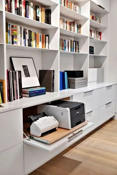 a white bookcase filled with books next to a printer on top of a desk