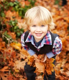 a young boy is smiling while standing in the leaves