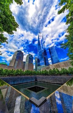 an artistic view of skyscrapers in the sky and reflecting pool with trees on either side