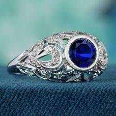 Add a delicate and unique aesthetic to your hand with this filigree ring crafted in elegant white gold, this exquisite ring showcases a breathtaking natural blue sapphire as its centerpiece. Intricate filigree detailing surrounding the sapphire enhances its allure, while multiple small diamonds adorn the ring, elevating its brilliance. With a design reminiscent of vintage elegance, this piece exudes timeless charm. Its beauty is truly captivating. CHARACTERISTICS Status: Made to order Origin: Th Fine Jewelry Sapphire Ring With Filigree, Elegant Sapphire Birthstone Ring For Promise, Elegant Royal Blue Sapphire Ring With Center Stone, Heirloom Blue Sapphire Ring With Diamond Accents, Exquisite Silver Sapphire Ring With Cubic Zirconia, Elegant Royal Blue Gemstone Rings, Anniversary Sapphire Ring With Filigree Fine Jewelry Style, Anniversary Fine Jewelry Sapphire Ring With Filigree, Luxury Blue Birthstone Ring For Wedding