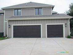 two garage doors are open in front of a large gray house with grass and trees