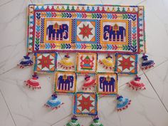 a colorful wall hanging with elephants and birds on it's sides, surrounded by tassels