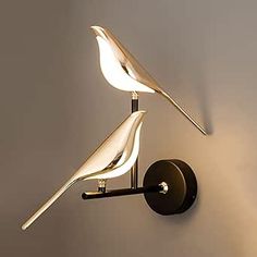 a white bird is sitting on top of a black wall light that is mounted to the side of a gray wall