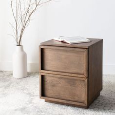 two drawers on the floor next to a vase with branches in it and a book on top