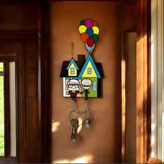 a house shaped clock hanging on the side of a wall with balloons attached to it