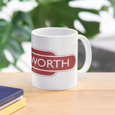 a white coffee mug sitting on top of a wooden table next to a book and plant