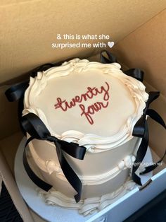 a white cake in a box with black ribbon and writing on the side that says twenty four