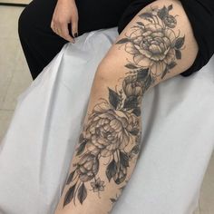 a woman sitting in a chair with flowers on her leg and arm tattooing it