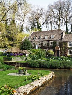 a large house sitting next to a river in front of a lush green field with lots of flowers