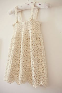 a white crocheted dress hanging on a clothes hanger next to a wall