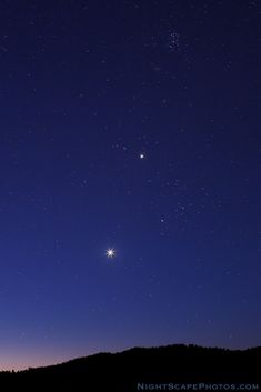 the night sky with two stars in it and one light shining on top of a hill