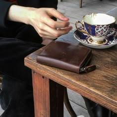 a person sitting at a wooden table with a cup and saucer on top of it