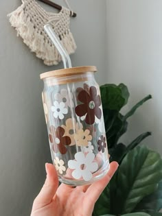 a person holding up a glass with flowers on it and a straw in the cup