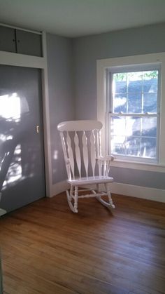 a white rocking chair sitting in front of a window next to a wooden floor with hard wood floors