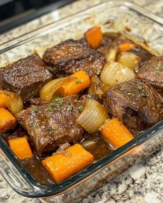 a glass dish filled with beef and carrots on top of a granite countertop