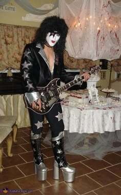 a man dressed in black and white holding a guitar while standing next to a table