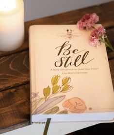 a book sitting on top of a wooden table next to a candle and some flowers