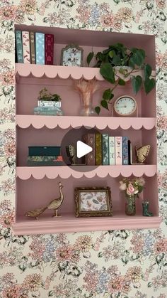 a pink shelf with books and other items on it in front of a floral wallpapered wall