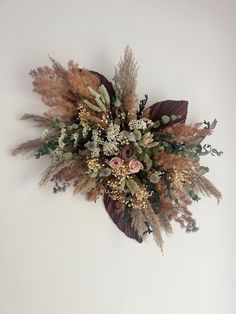 an arrangement of dried flowers and foliage on a white wall