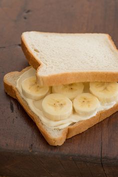 a sandwich with sliced bananas and cream cheese on it sitting on top of a wooden table